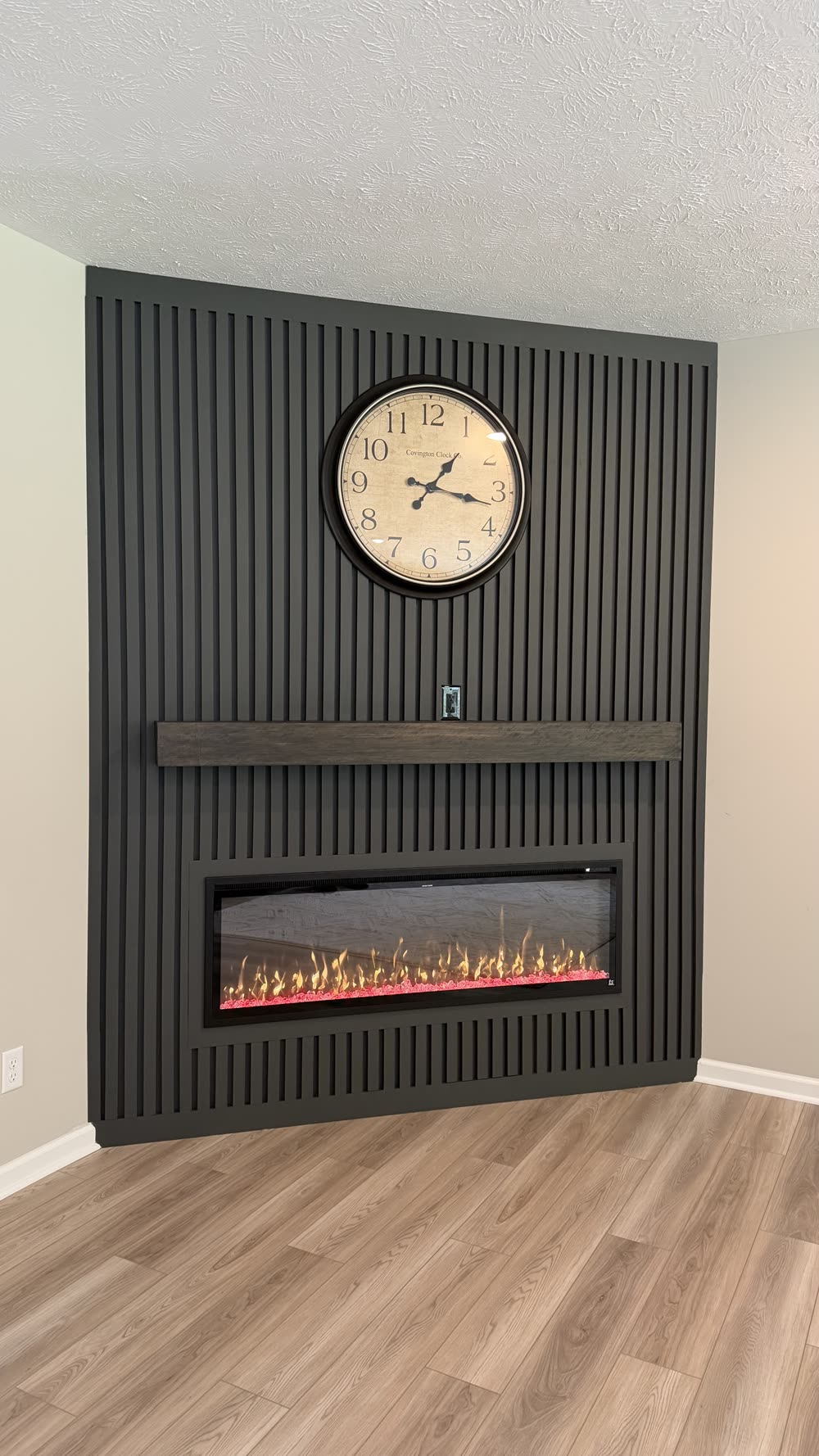 Black vertical slat wall with wall clock, floating mantel, and fireplace, no TV